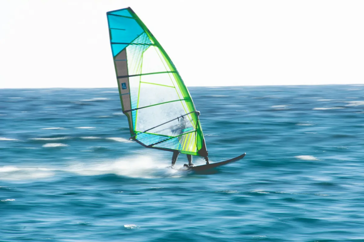Windsurfeur filant sur une mer bleue sous une voile verte et bleue, image légèrement floue par le mouvement