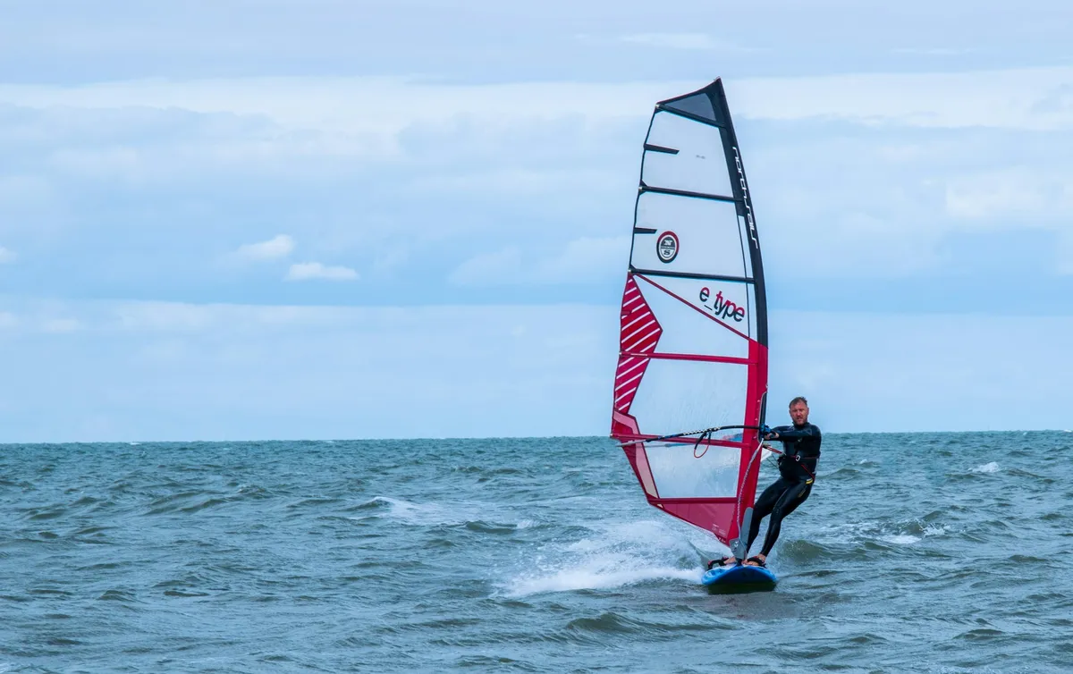 A windsurfer planing on choppy water with a wake of spray behind the board