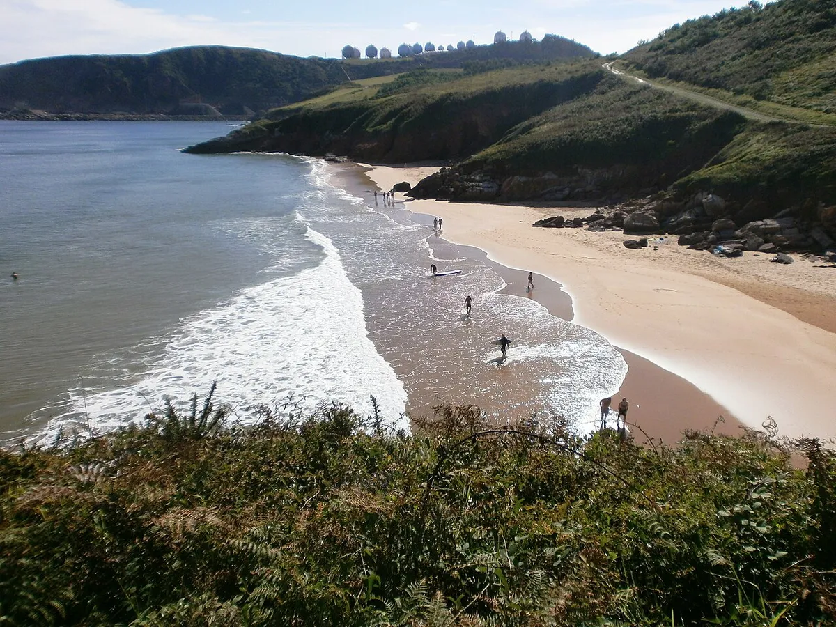 Playa de Xivares, en Carreño: arenal entre laderas verdes, con gente en la orilla y el mar abierto