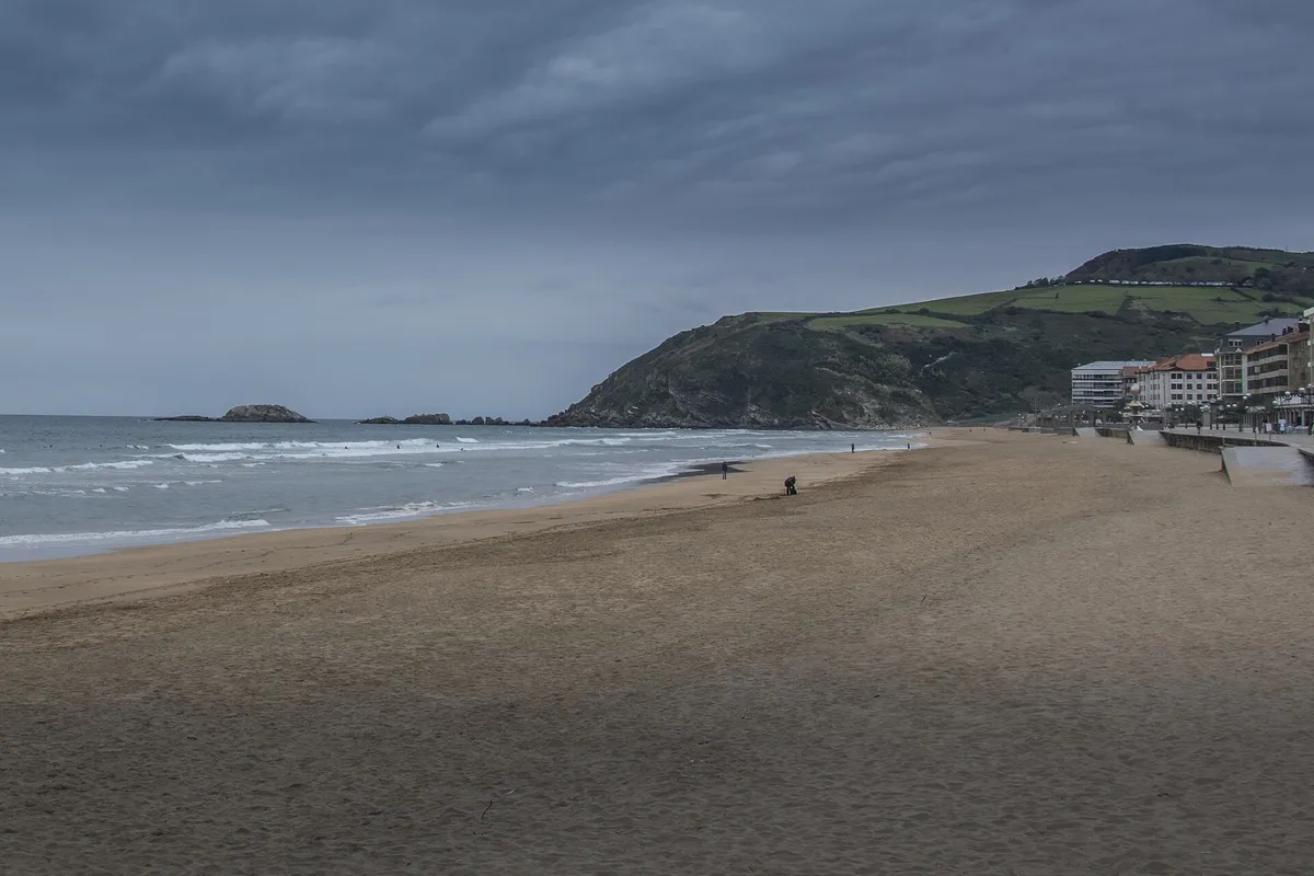 Playa de Zarautz con el pueblo y un promontorio verde al fondo, bajo un cielo nublado