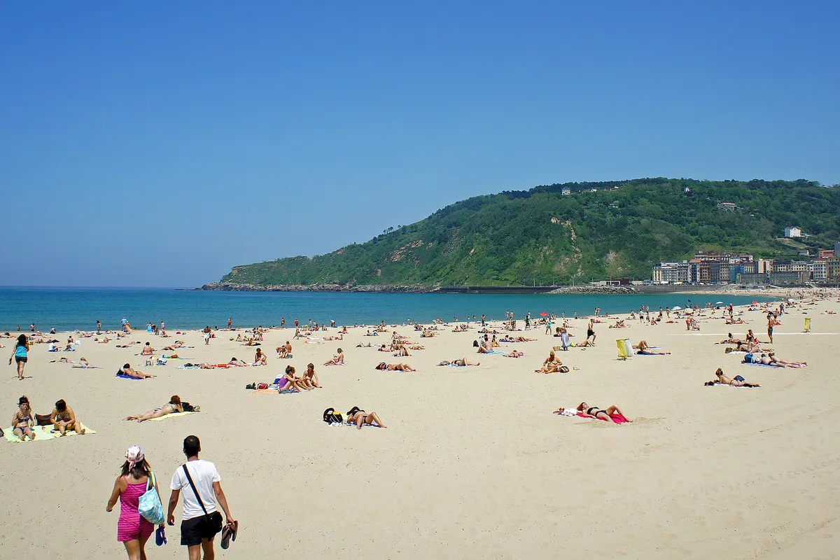 Zurriola beach in San Sebastián on a summer day, with sunbathers on the sand and a green headland behind