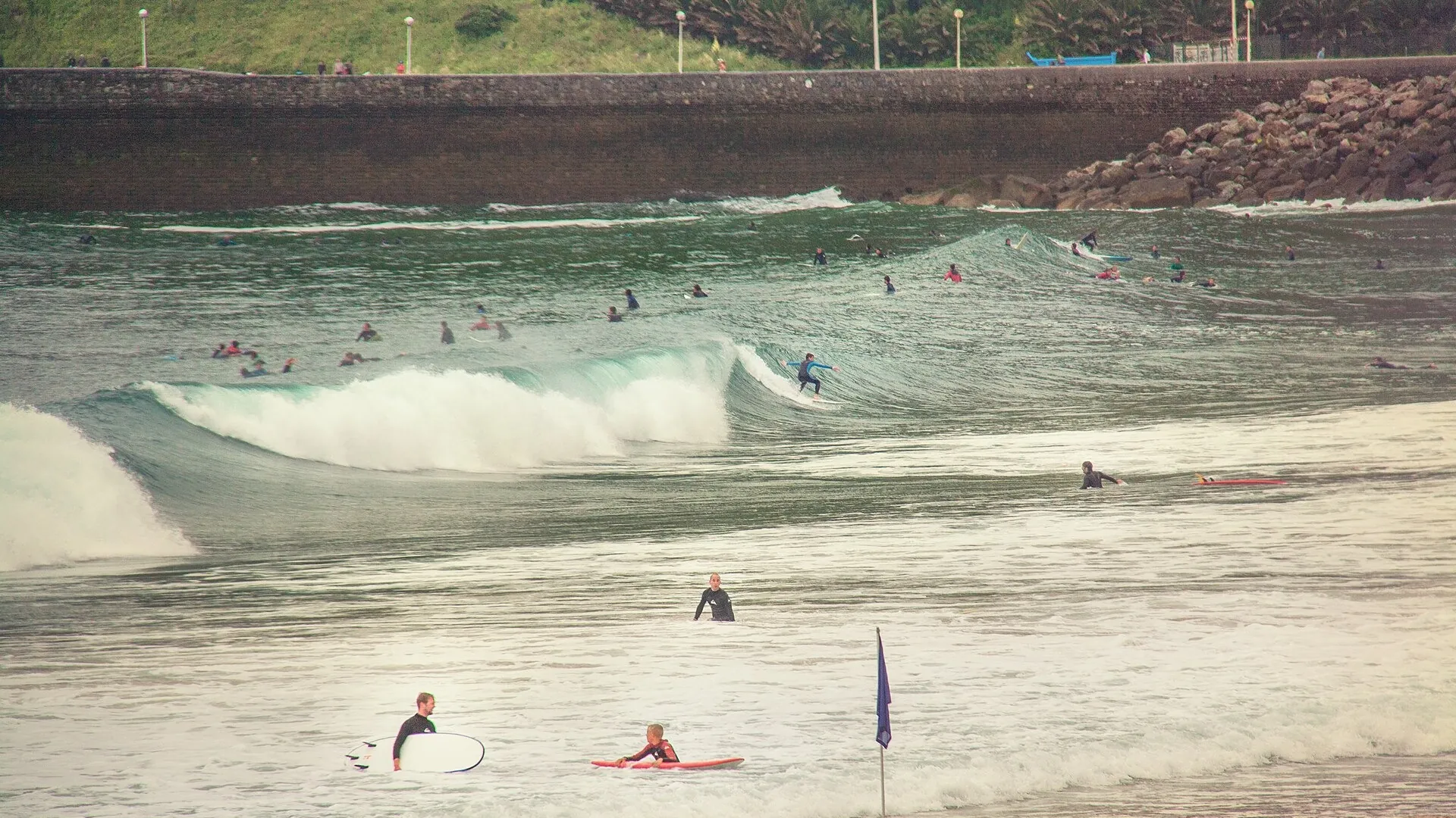 Surfers in the lineup at Zurriola beach, San Sebastián, with the sea wall and breakwater behind them